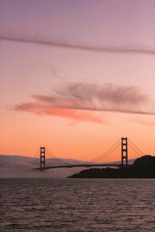 a large body of water with a bridge in the background, by Dave Melvin, unsplash, romanticism, orange / pink sky, golden gate, photo taken from a boat, taken in the late 2000s