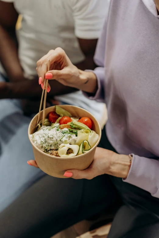 a woman holding a bowl of food with chopsticks, sustainable materials, square, foam, salad