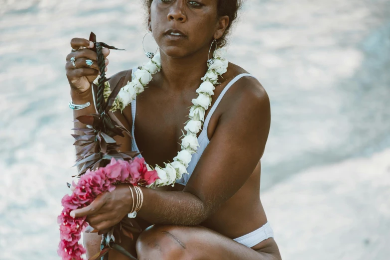 a woman sitting on a rock with a flower garland around her neck, pexels contest winner, hurufiyya, puka shell necklace, tanned skin, mid 2 0's female, holding a trident