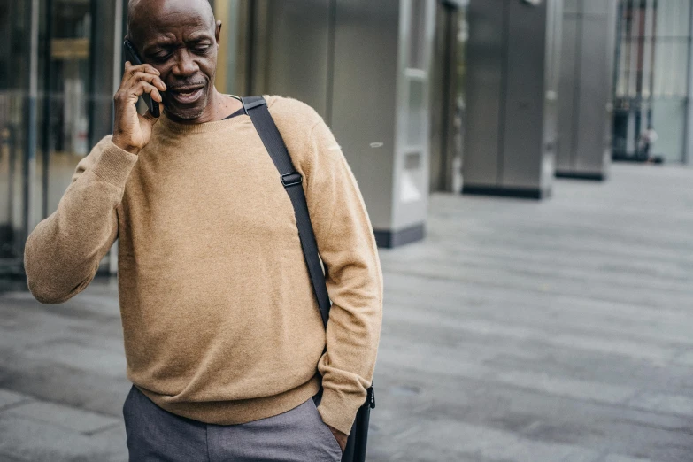 a man walking down a street talking on a cell phone, a photo, muted brown yellow and blacks, an oldman, portrait featured on unsplash, brown clothes