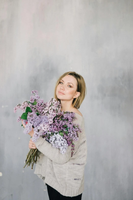 a woman holding a bunch of purple flowers, inspired by Ilka Gedő, pexels contest winner, light grey backdrop, russian girlfriend, celebration, february)