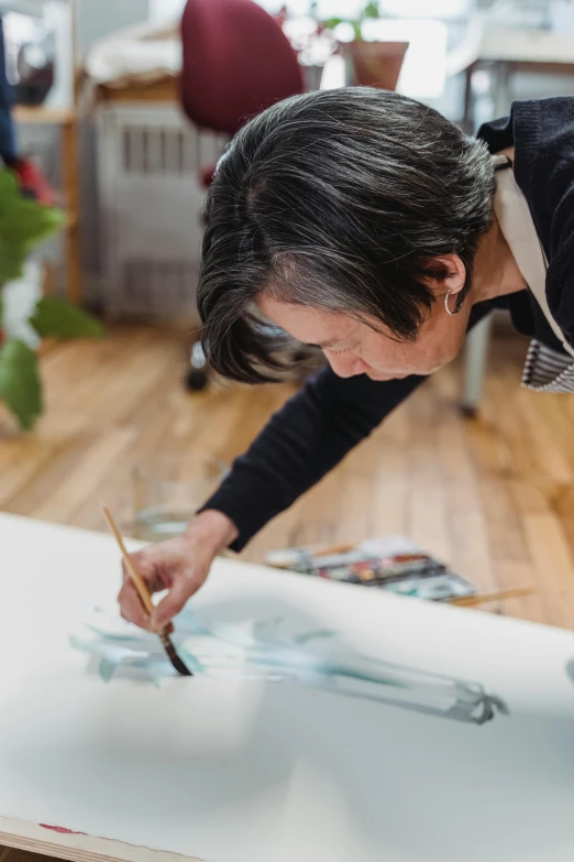 a woman is painting a picture on a canvas, a photorealistic painting, by Miyamoto, leaning towards watercolor, shodo, grey, collaborative