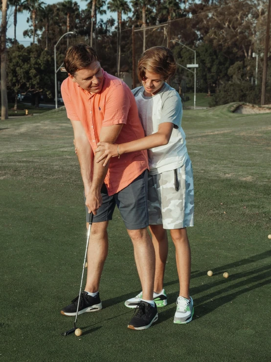 a couple of people standing on top of a green field, wearing golf shorts, supportive, aged 13, thumbnail