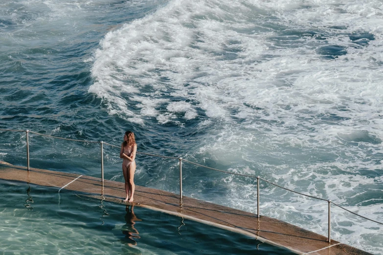 a woman standing on a pier next to a body of water, happening, luxurious onsens, manly, whirlpool, high angle