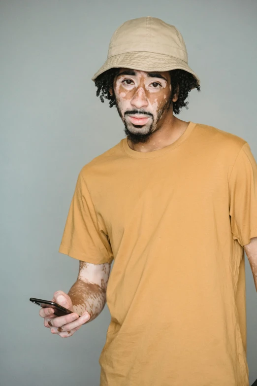 a man wearing a hat and holding a cell phone, by Stokely Webster, wearing a modern yellow tshirt, deteriorated, ashteroth, medium skin tone