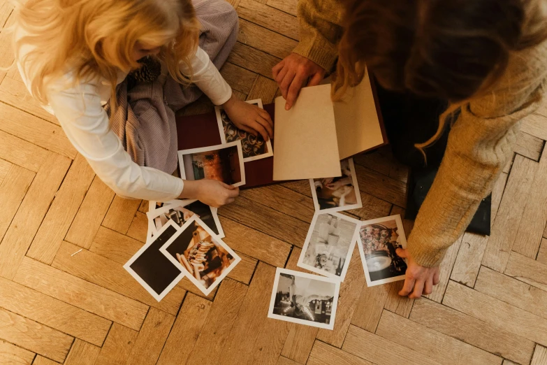 a couple of women sitting on top of a wooden floor, a polaroid photo, by Emma Andijewska, pexels contest winner, families playing, inspect in inventory image, old photobook, in a wooden box. top down photo