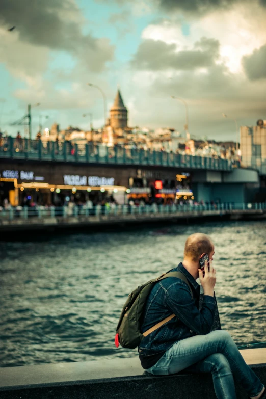 a man sitting on a wall talking on a cell phone, by irakli nadar, pexels contest winner, happening, photo taken from a boat, turkish and russian, a man wearing a backpack, brown