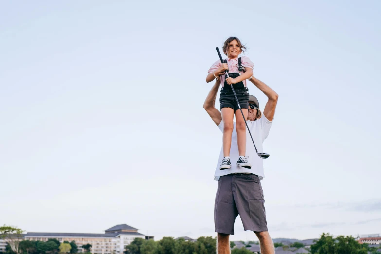 a man holding a little girl up in the air, by Lee Loughridge, pexels contest winner, golf course in background, minn, clubs, manuka