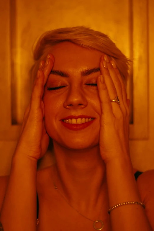 a woman holding her hands to her face, an album cover, inspired by Elsa Bleda, massurrealism, red door blonde, happy cozy feelings, warm yellow lights, movie filmstill