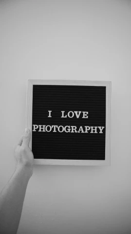 a person holding up a sign that says i love photography, a black and white photo, photograph”, display”, - i, minimalist photo