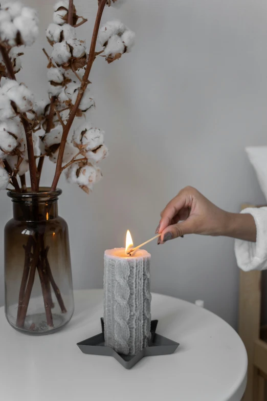 a person lighting a candle on a table, inspired by Kim Tschang Yeul, light grey, indoor picture, winter season, close angle