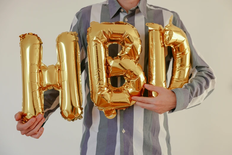 a man in a striped shirt holding up gold balloons, unsplash, hyperrealism, detailed letters, h3h3, happy birthday, inhabited initials