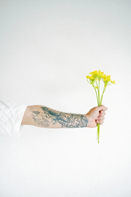 a person holding a bunch of yellow flowers, a tattoo, by Jessie Alexandra Dick, unsplash, minimalism, prosthetic arm, white sleeves, tattoo parlor photo, profile image