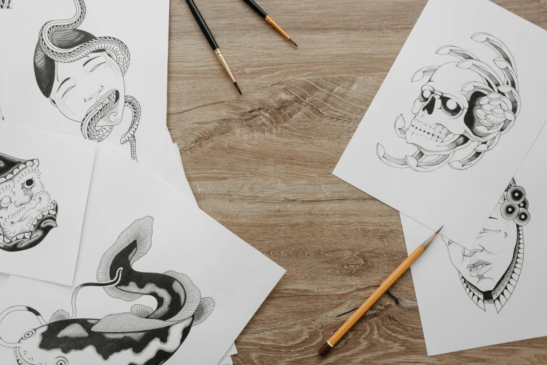a bunch of drawings sitting on top of a wooden table, an ink drawing, inspired by Kawanabe Kyōsai, trending on pexels, animal skull, graphic templates, drawing 4k, tattoo sketch of a ocean
