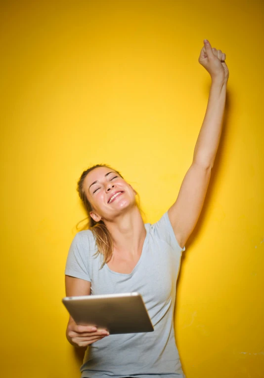 a woman standing in front of a yellow wall with her arms in the air, happening, using a macbook, celebrate goal, digital image, full frame image