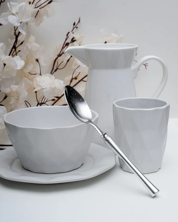 a white table topped with cups and saucers, spoon, on grey background, titanium white, silver insignia