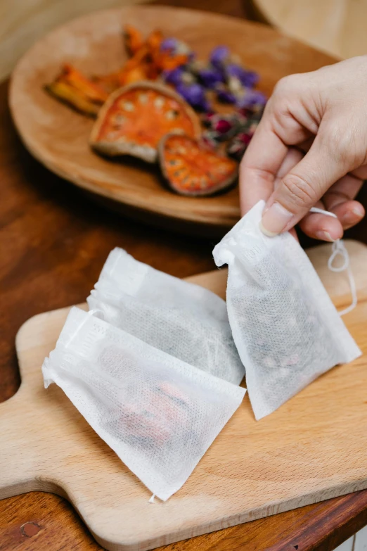 two bags of tea sitting on top of a wooden cutting board, by Jessie Algie, unsplash, made of lab tissue, hands on counter, detailed product image, half image