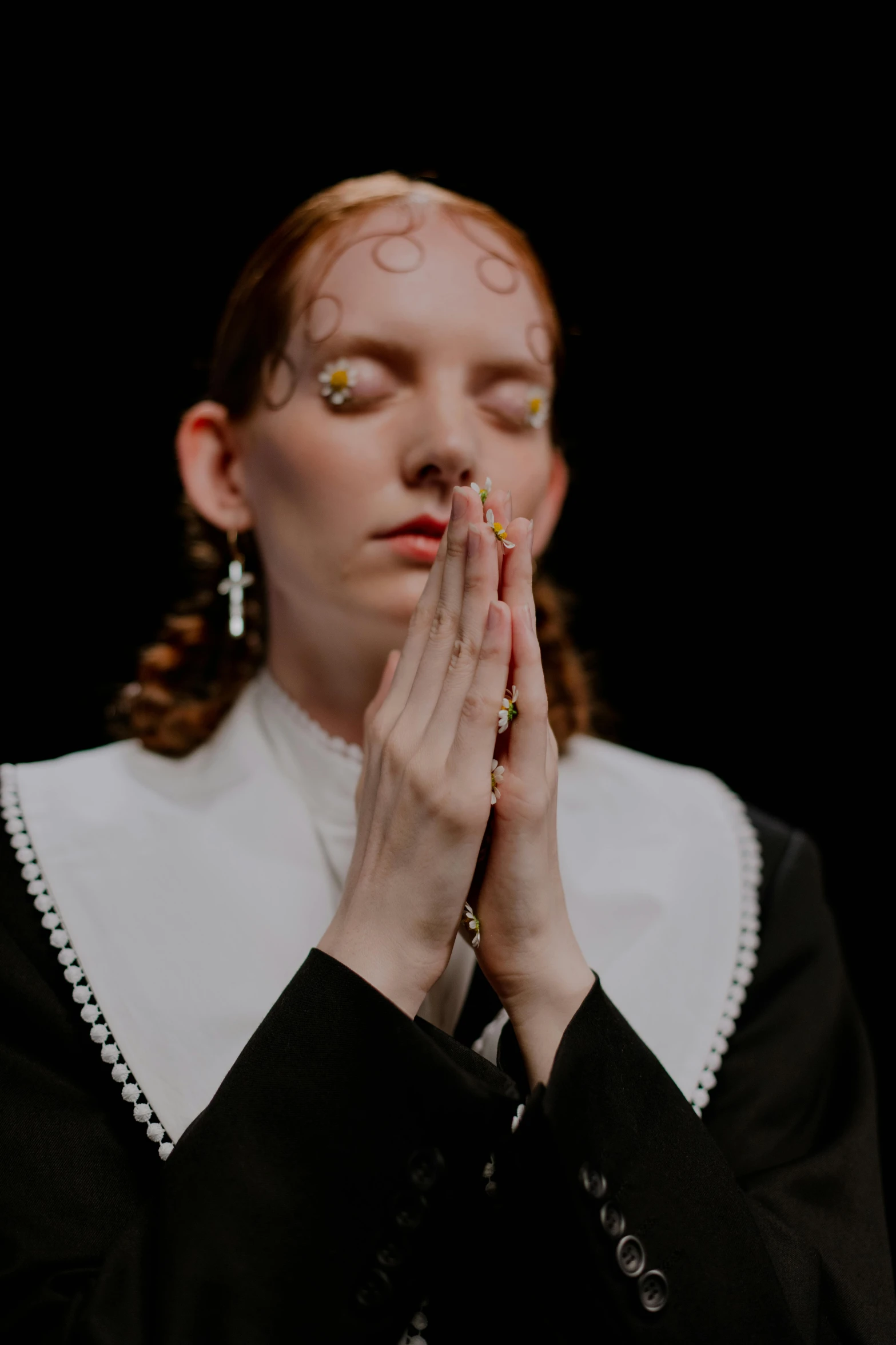 a woman with her eyes closed in prayer, an album cover, inspired by Lucas Cranach the Elder, trending on unsplash, dressed like a cleric, huge earrings and queer make up, blessing hands, showstudio