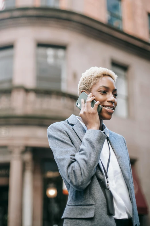 a woman talking on a cell phone in front of a building, trending on pexels, short blonde afro, corporate phone app icon, non-binary, historical