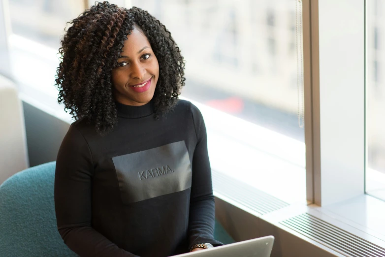 a woman sitting in a chair with a laptop, by Arabella Rankin, pexels contest winner, hurufiyya, panel of black, vp of marketing, standing near a window, karma