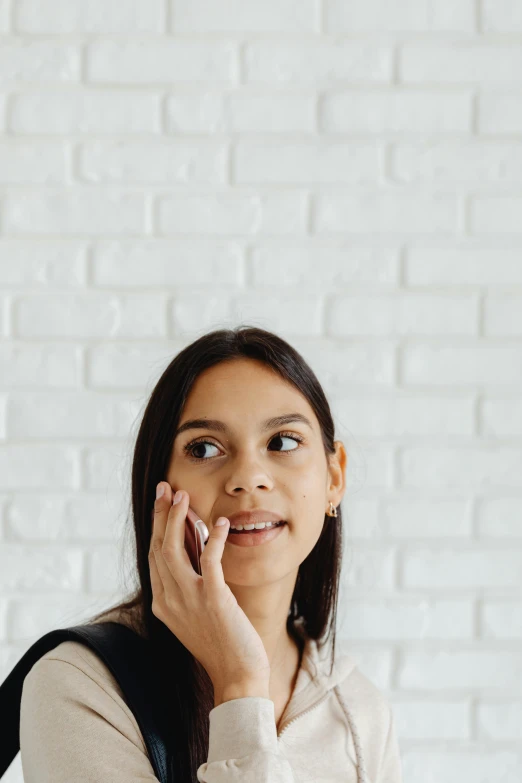 a woman talking on a cell phone in front of a brick wall, trending on pexels, hypermodernism, white backdrop, indian girl with brown skin, square jaw-line, looking surprised