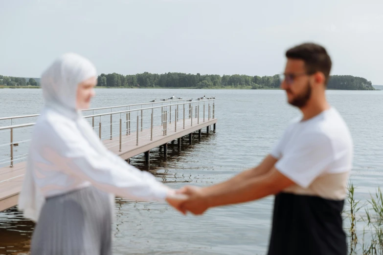 a man and a woman shaking hands in front of a body of water, by Julia Pishtar, hurufiyya, hijab, near a jetty, aleksander rostov, high quality image