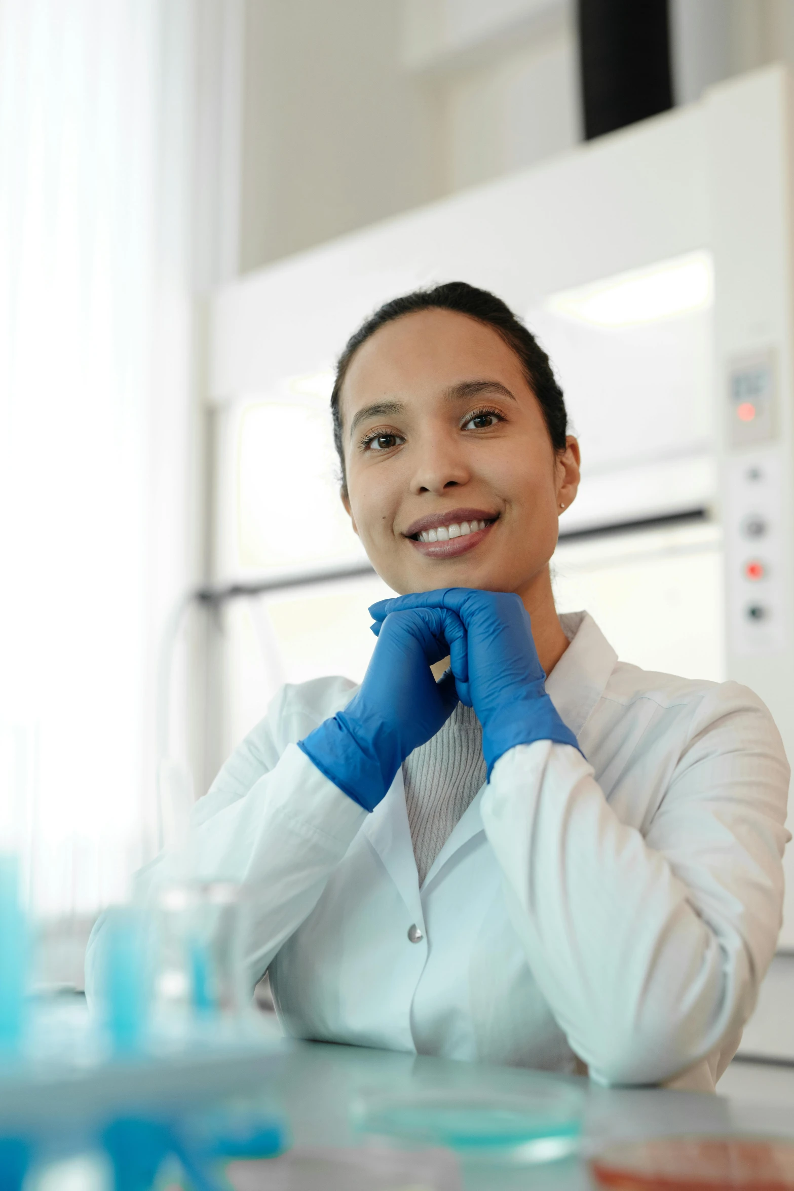 a woman in a lab coat sitting at a table, a portrait, shutterstock, wearing gloves, confident smile, up close, high quality picture