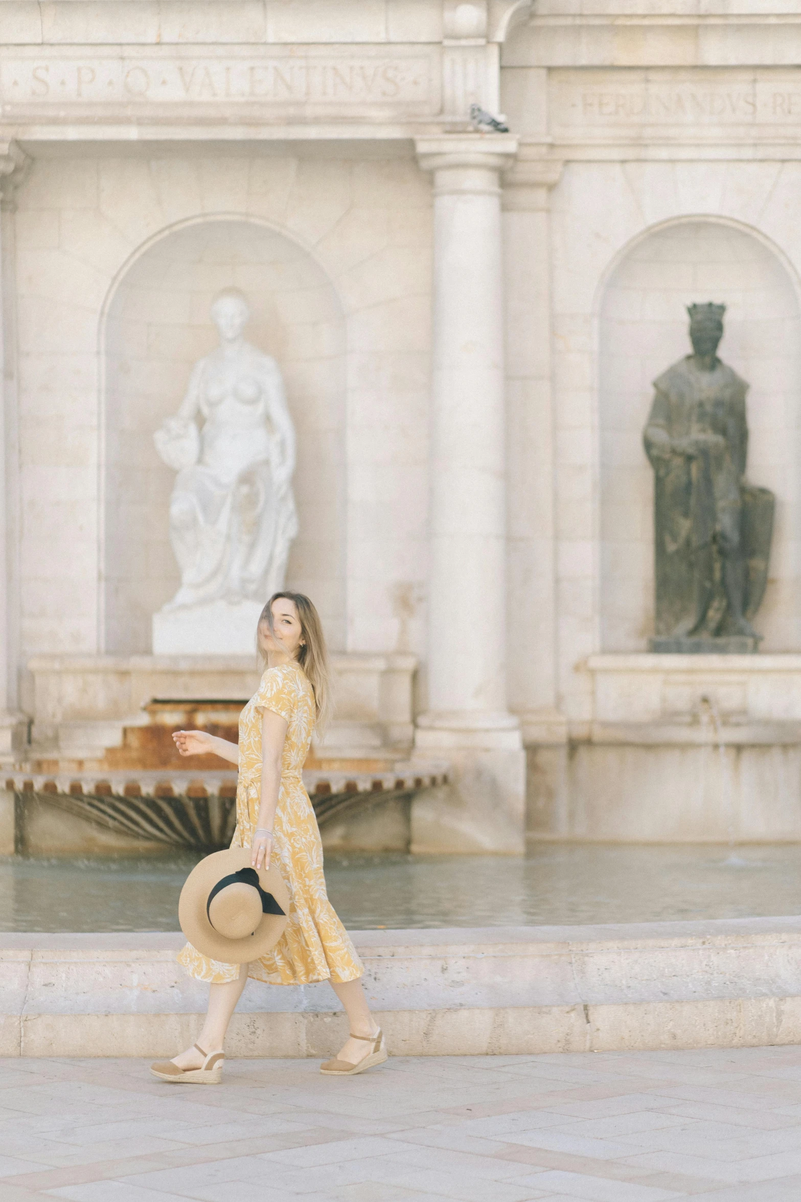 a woman in a yellow dress walking in front of a fountain, a marble sculpture, trending on unsplash, classical robes, wearing straw hat, marie - gabrielle capet style, patterned clothing