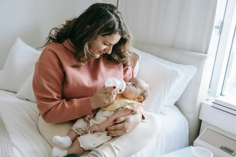 a woman sitting on a bed feeding a baby, pexels contest winner, happening, holding a drink, manuka, avatar image, 1 2 9 7