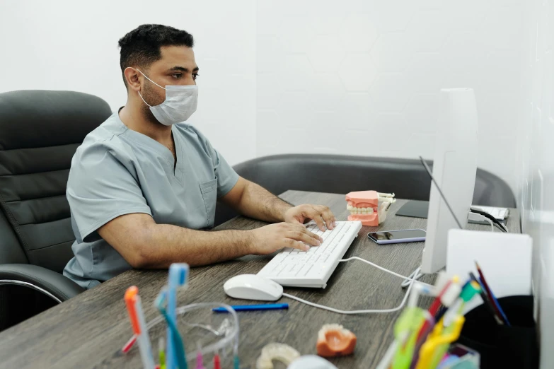 a man sitting at a desk in front of a computer, uniform teeth, colour corrected, masked doctors, profile image