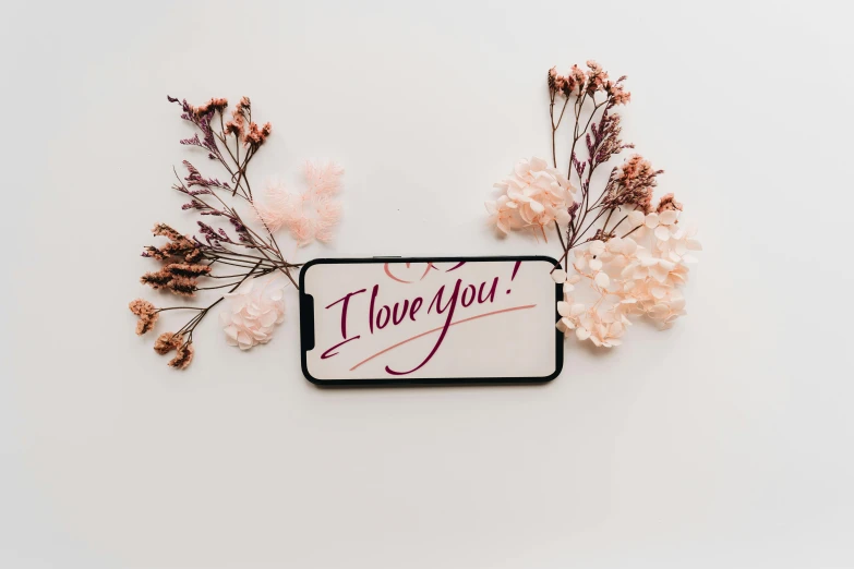 a phone with the words i love you written on it, trending on pexels, flower frame, set against a white background, background image, uploaded