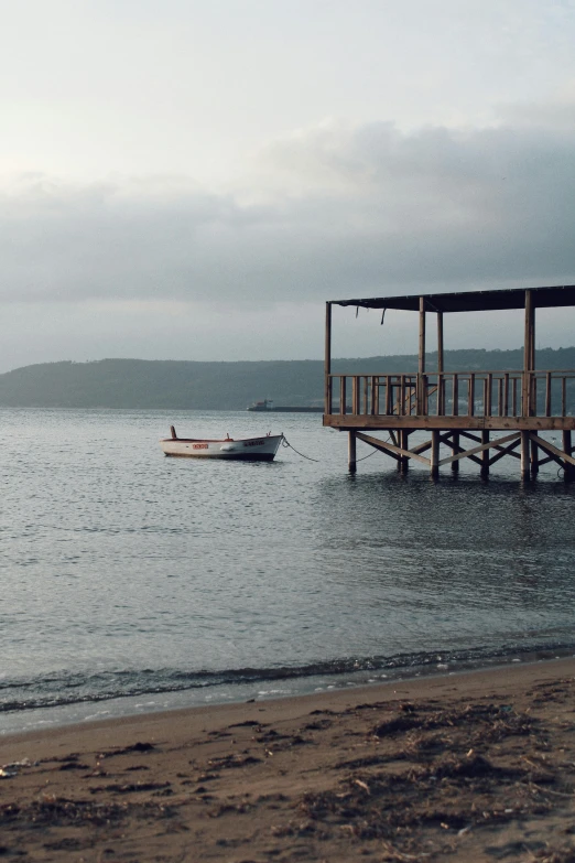 a boat sitting on top of a body of water, dau-al-set, beach bar, gray skies, wooden structures, late afternoon