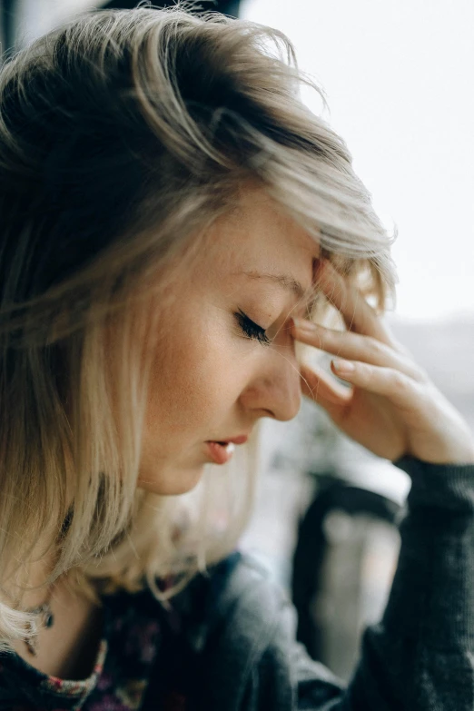 a woman sitting at a table with her head in her hands, pexels, close up of a blonde woman, hurting, showing forehead, walking down