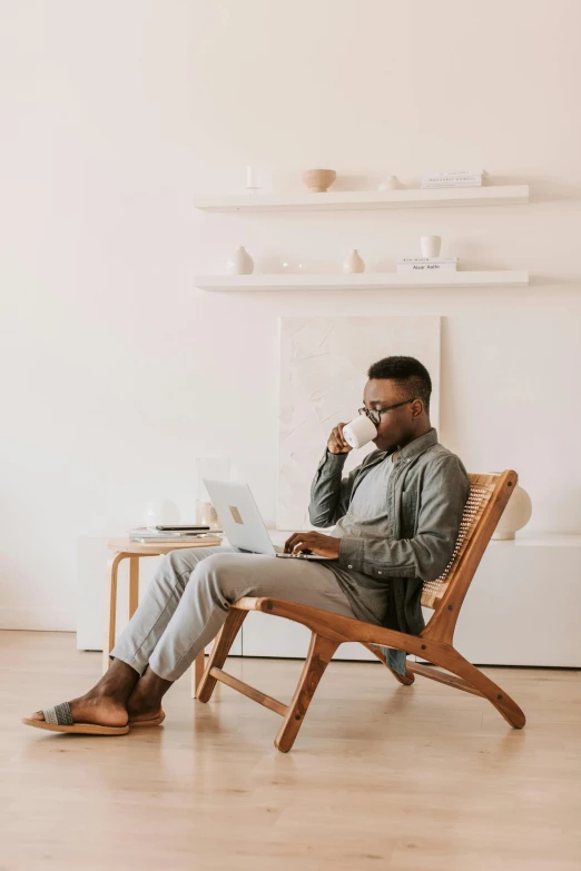 a man sitting in a chair using a laptop, pexels contest winner, drinking tea, sitting in an empty white room, black man, sitting in fancy chair