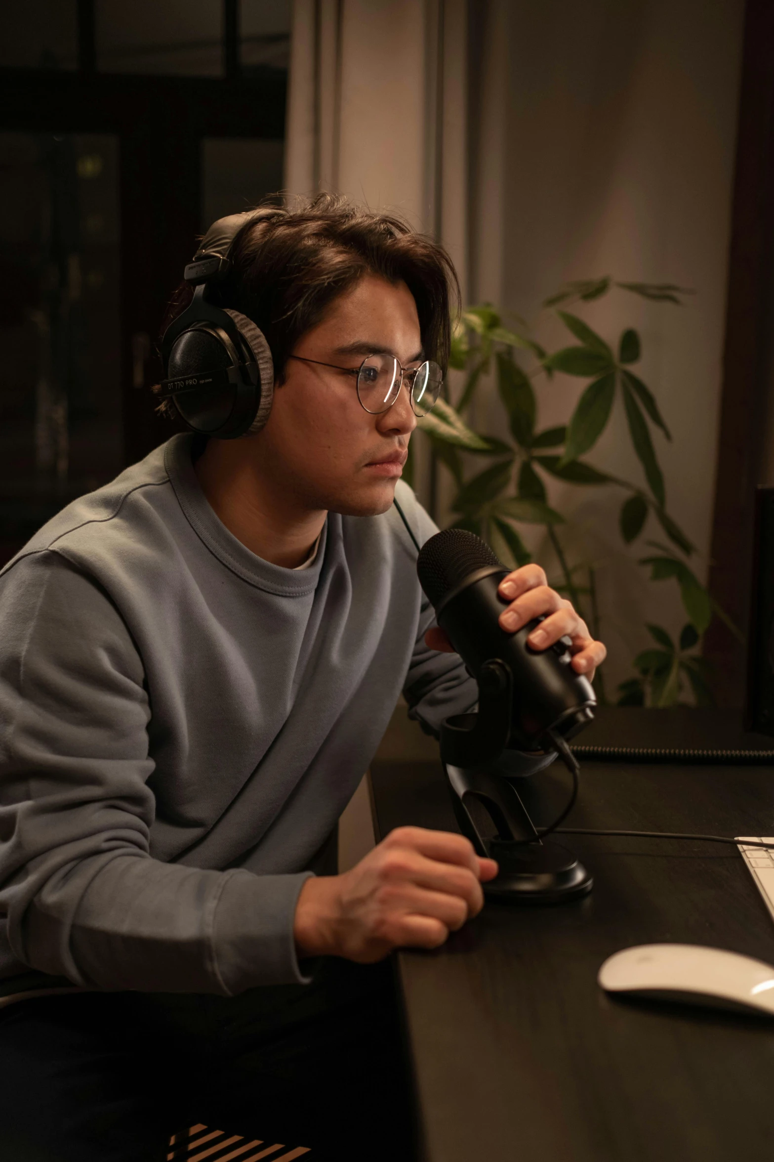 a man sitting at a desk in front of a computer, by Jang Seung-eop, rapping into microphone, avan jogia angel, with head phones, with glasses