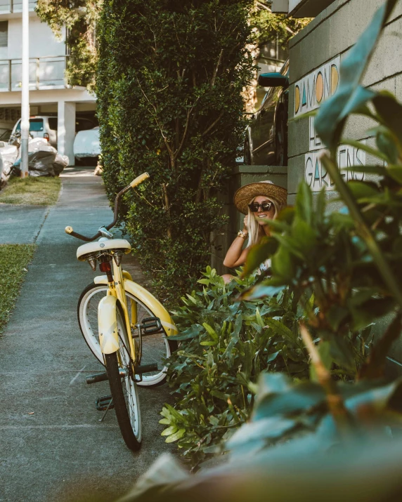 a woman sitting on a sidewalk next to a bike, by Carey Morris, pexels contest winner, lush greenery, white and yellow scheme, profile image, tourist photo