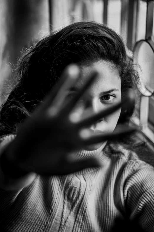 a black and white photo of a girl looking out a window, by Alexis Grimou, pexels contest winner, hands shielding face, with violence, wave a hand at the camera, photo of young woman