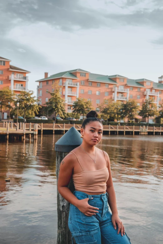 a woman sitting on a dock next to a body of water, in savannah, mixed-race woman, profile image, waterfront houses