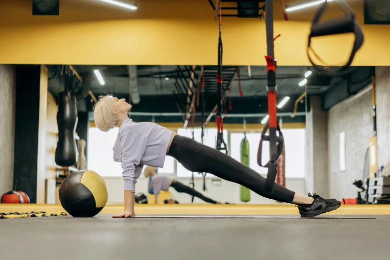 a woman doing push ups with a medicine ball, a photo, by Matija Jama, trending on pexels, arabesque, black and yellow and red scheme, hanging from the ceiling, sydney hanson, central hub