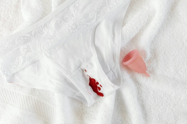 a pair of underwear sitting on top of a bed, a still life, trending on pexels, blood drop, white and pink, speculum, made of blood