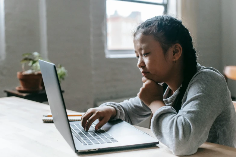 a woman sitting at a table using a laptop computer, trending on pexels, tiny girl looking on, south east asian with round face, aged 13, no watermark