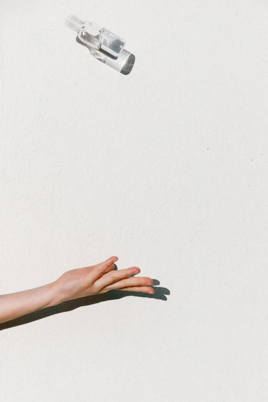 a woman reaching out to catch a bottle of soda, unsplash, minimalism, white concrete, ✨🕌🌙, wall, on a sunny day