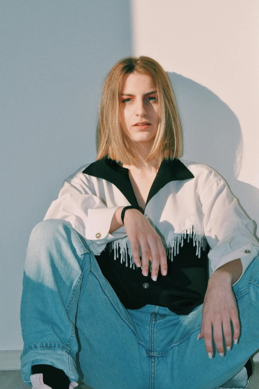 a woman sitting on the ground with her legs crossed, an album cover, inspired by Elsa Bleda, trending on pexels, photorealism, sleek blond hair, portrait androgynous girl, in white room, baggy jeans