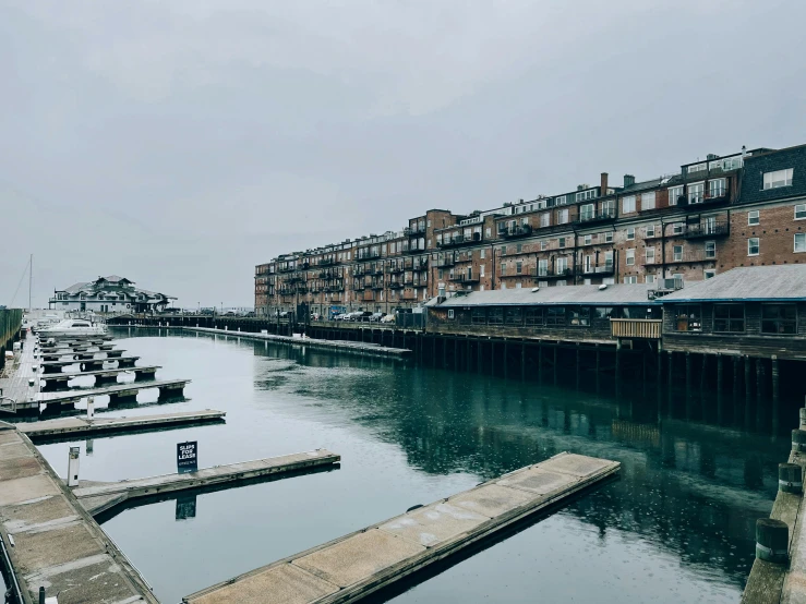 a marina filled with lots of boats next to tall buildings, by Washington Allston, unsplash, hurufiyya, wood pier and houses, overcast day, william warehouse, seen from outside