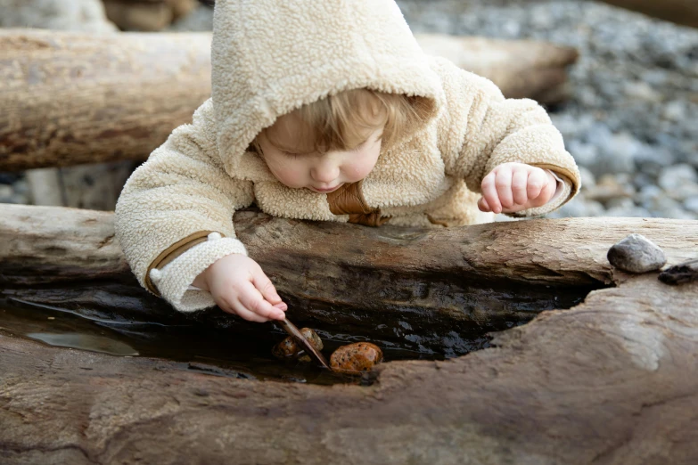 a small child standing on top of a log, inspired by Andy Goldsworthy, unsplash, brown hooded cloak, playing with the water, fossil ornaments, eating