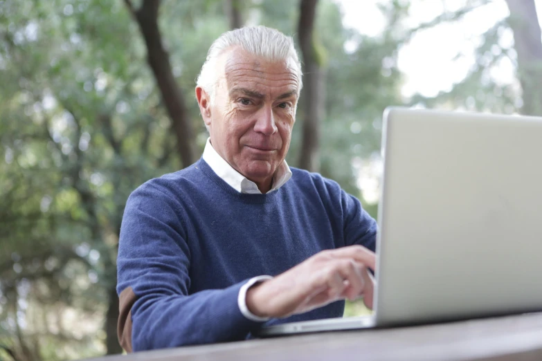 a man sitting at a table using a laptop computer, by Harriet Zeitlin, pexels, white haired, outside, brown, gray haired