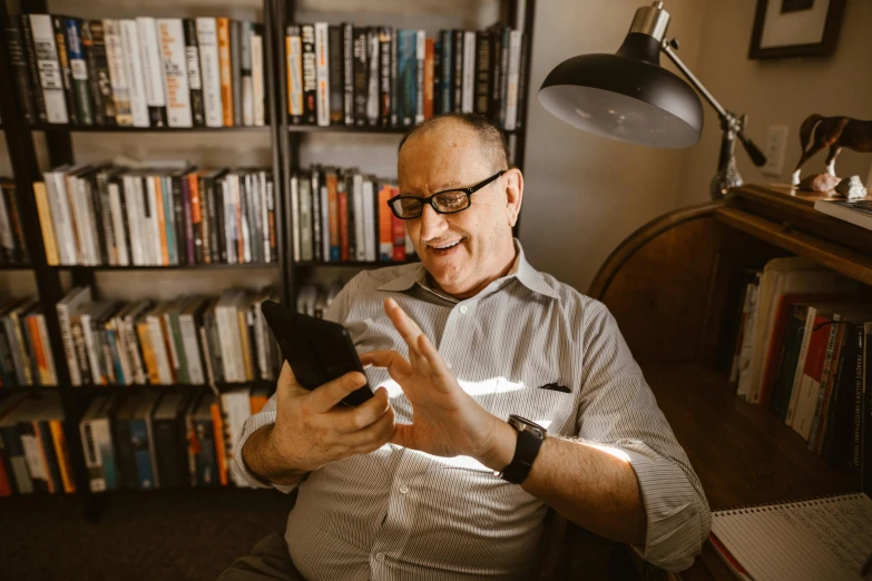 a man sitting in a chair looking at a cell phone, wearing reading glasses, a still of a happy, abcdefghijklmnopqrstuvwxyz, best photo