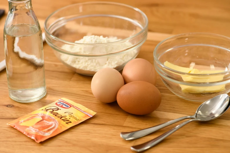 a wooden table topped with bowls of food and a bottle of water, eggs, detailed product image, yeast, baking a cake