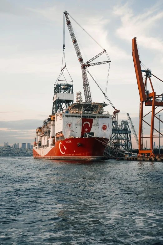 a red and white boat in a body of water, sitting in a crane, on the ocean, industries, gold pipelines