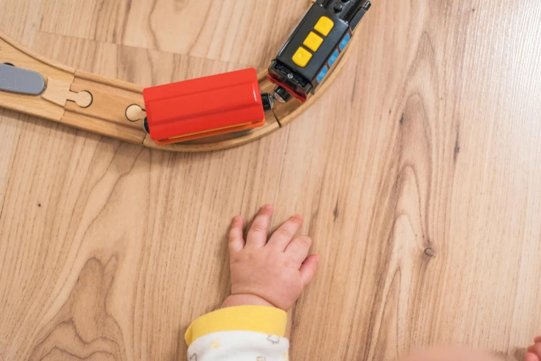 a child playing with a train set on a wooden floor, bump in form of hand, subtle detailing, wood effect, multi - coloured